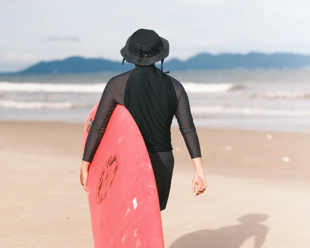 A wetsuited surfer carries a red board toward the waves.