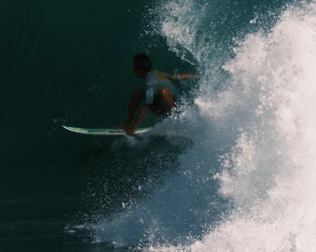 A surfer rides low beneath a breaking wave.