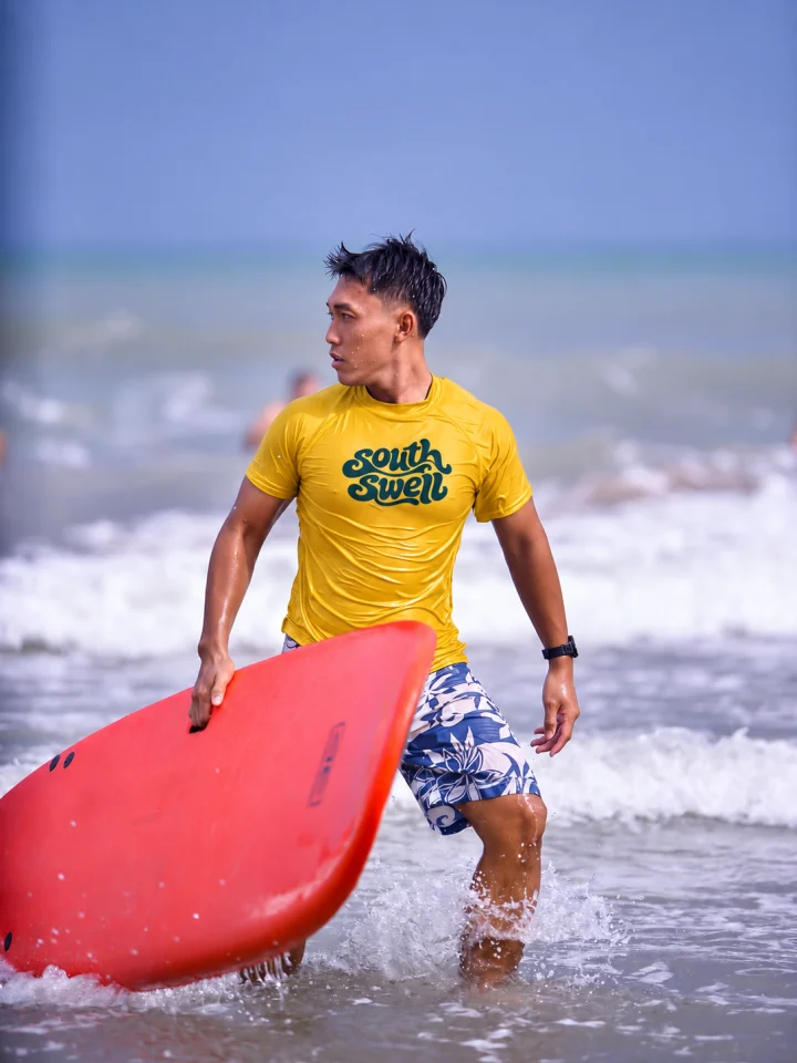 Hoàng carrying a red surfboard in the shore break.