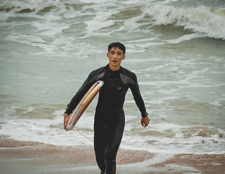 Yuki carrying a surfboard out of the shore break.