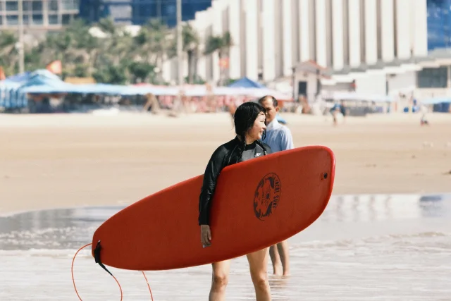A surfer carrying a red board at the shoreline.