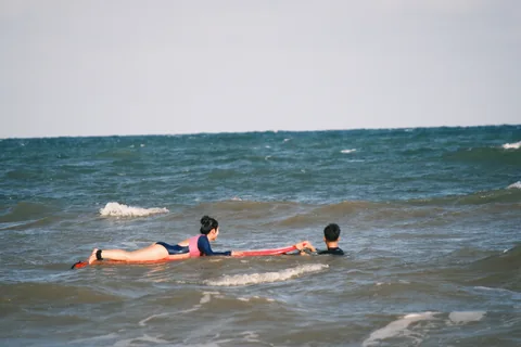 A coach stays beside a student practising paddling in shallow water.
