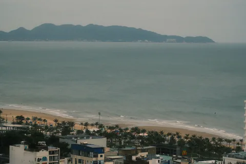 A sandy bay and coastal rooftops seen from the hillside.
